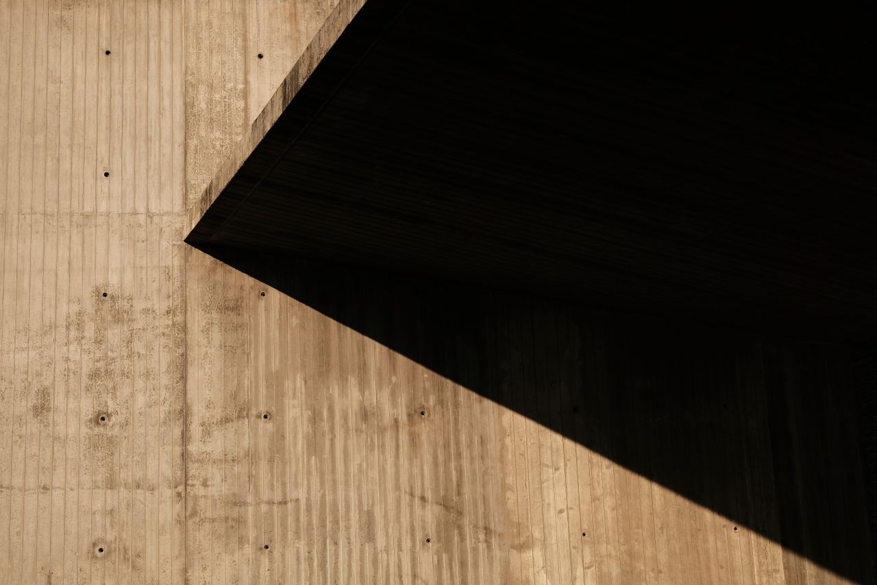 Offerings Abstract view of a concrete wall with contrasting shadows and geometric design elements.