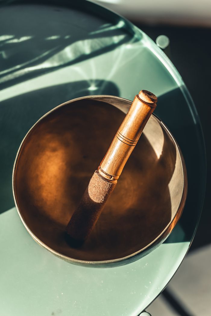 Offerings A Tibetan singing bowl with a wooden mallet placed on a green surface, illuminated by sunlight.